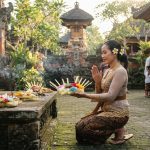 Wanita Bali mengenakan kebaya sedang berdoa di pura dengan persembahan canang sari
