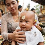 Seorang ibu di Bali memakaikan hiasan bawang putih di dahi bayinya saat upacara di pura.