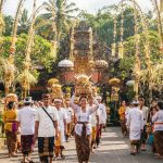 Suasana perayaan Galungan di sebuah pura di Bali dengan penjor dan umat Hindu berbaju adat berjalan beriringan.